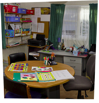 The teaching room, with a table, desk and various educational posters and material visible
